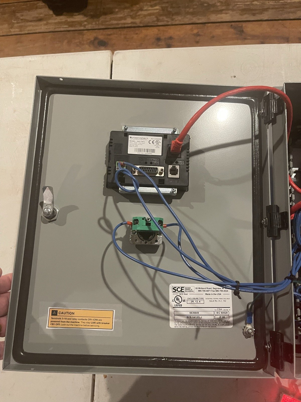 Back of the panel door showing the touchscreen, pushbutton contact block, and caution label